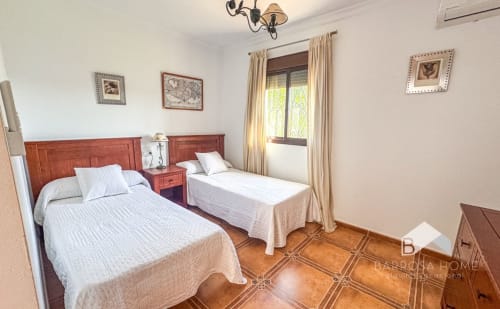 Dormitorio doble en Villa Alba Barrosa con camas de madera, suelos de terracota y vistas al jardín en España