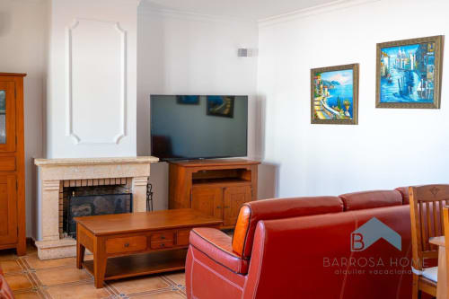 Amplio salón en villa Barrosa Home con sofá de cuero rojo, chimenea, TV, muebles de madera y estilo mediterráneo costero