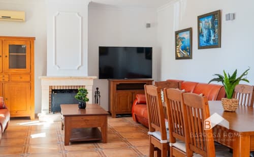Sala de estar de la Villa Alba en Barrosa Home con muebles de madera, sofá naranja, chimenea y televisor