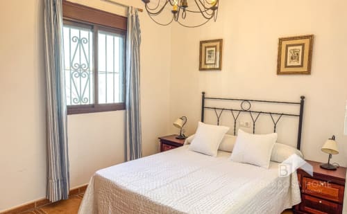Dormitorio de Villa Alba en Barrosa Home con cama de hierro forjado, ropa de cama crema, mesitas de madera y puerta de balcón decorativa