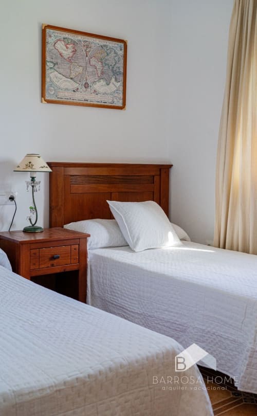 Dos camas gemelas con sábanas blancas en villa Barrosa Home, mesita de noche de madera con lámpara y mapa mundi antiguo en la pared