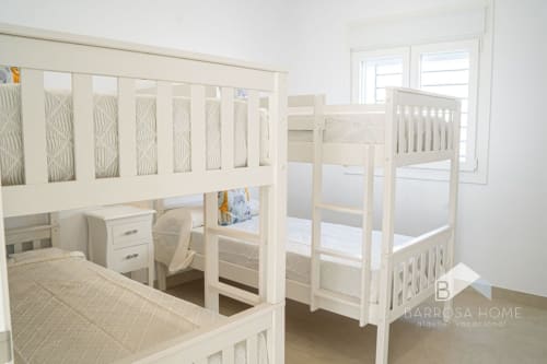 Luminosa habitación infantil en villa Barrosa Home con camas literas blancas, cunas y luz natural de las ventanas