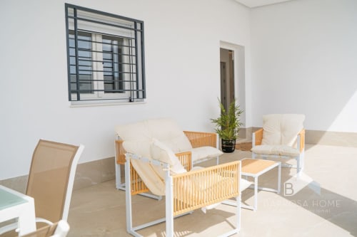 Zona de estar moderna en Villa Horizonte de Barrosa Home con muebles de madera, cojines crema y paredes blancas minimalistas