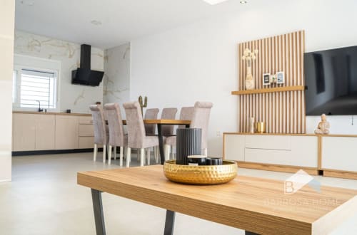 Amplia sala de estar con plano abierto en villa Barrosa Home, con mesa de madera, sillas de comedor, cocina y TV de pared