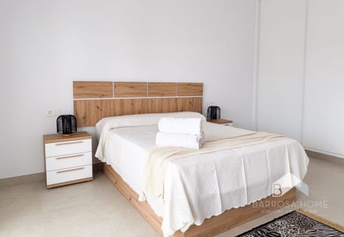 Dormitorio moderno en villa Barrosa Home con cama de madera, ropa de cama blanca y decoración minimalista en España