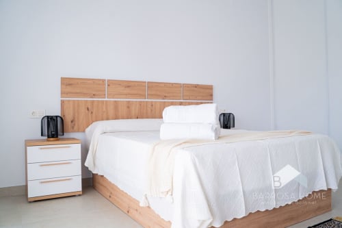 Dormitorio moderno en villa Barrosa Home con cama de madera, ropa de cama blanca, mesita de noche y decoración minimalista