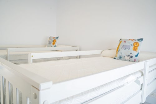 Camas gemelas con marcos de madera blanca, almohadas con estampados de animales coloridos y ropa de cama neutra en la villa Barrosa Home en España
