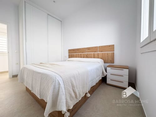 Dormitorio moderno en villa Barrosa Home con cama de madera, ropa blanca, mesita de noche y decoración minimalista