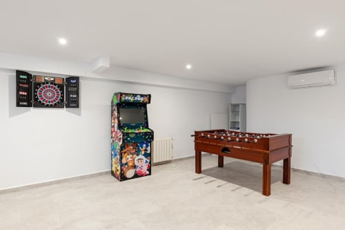 Sala de juegos en Barrosa Home con máquina de arcade, futbolín, diana y paredes blancas modernas