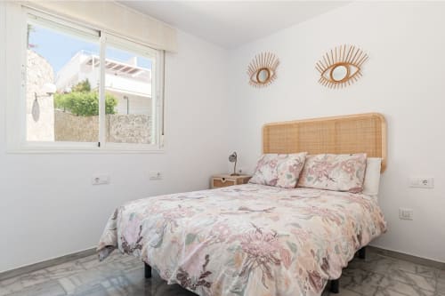 Dormitorio moderno en Barrosa Home con cabecero de ratán, ropa de cama floral, arte mural y luz natural