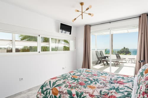 Luminoso dormitorio en Barrosa Home con ropa de cama floral, vista al mar, acceso a balcón e iluminación moderna
