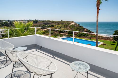 Terraza del apartamento Barrosa Home con tumbonas blancas, vista a la piscina y línea costera del Algarve frente al azul mar Mediterráneo