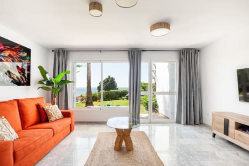 Luminoso salón moderno en Barrosa Home con sofá naranja, vistas al mar por puertas de cristal y detalles de madera