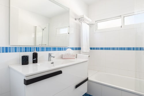 Baño moderno de Barrosa Home con azulejos blancos, detalles en azul rayado, lavamanos, espejo y bañera con ducha