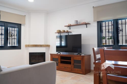 Moderna sala de estar en la villa Barrosa Home con chimenea, televisor, muebles de madera y ventanas con marco azul
