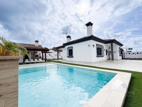 Villa Barrosa con piscina color turquesa, arquitectura blanca, palmeras y zona de descanso en España