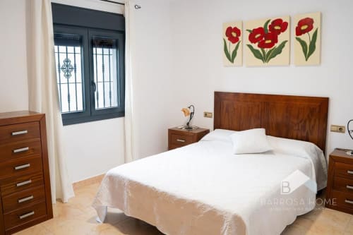 Dormitorio luminoso en villa Barrosa Home con cama de madera, ropa de cama blanca, mesitas de noche y arte floral rojo sobre el cabecero