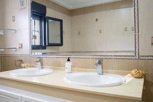 Baño moderno de la villa Barrosa Home con doble lavabo, encimera de mármol y azulejos beige