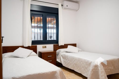 Dormitorio doble en villa Barrosa Home con camas de madera, ropa de cama blanca y puertas de terraza con vistas al mar