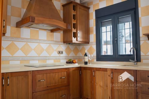 Elegante cocina en villa Barrosa Home con muebles de madera, encimera crema, azulejos geométricos y marco azul