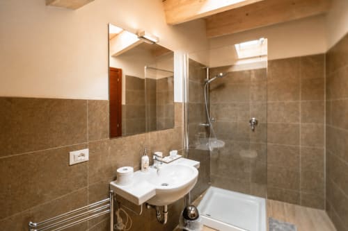Bagno moderno della Luxury Suite Al Battistero a Ravenna con lavabo curvo bianco, box doccia in vetro e pareti in piastrelle marrone