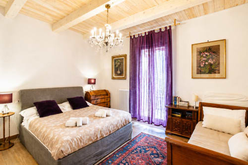 Elegante suite presso Al Battistero a Ravenna con letto matrimoniale, tende viola, travi in legno e vista sul giardino