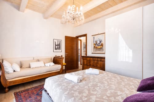 Elegante suite di Al Battistero a Ravenna con travi in legno, lampadario, letto con lenzuola bianche e divano beige con vista sul giardino