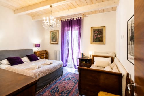 Suite elegante all'Al Battistero di Ravenna con tende viola, travi in legno, lampadario di cristallo e vista sul giardino