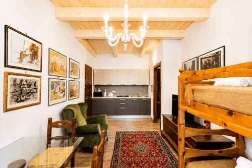 Suite Lusso Al Battistero a Ravenna: ampia suite con angolo cottura, travi in legno, poltrona verde, letto a castello e opere d'arte