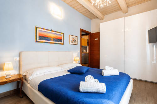 Camera moderna presso Al Battistero Luxury Suite a Ravenna con biancheria blu, testata bianca, travi in legno e vista sulla città