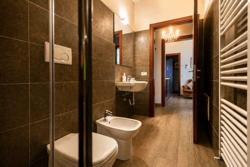 Bagno moderno nella Luxury Suite Al Battistero di Ravenna con piastrelle scure, toilette, bidet, doppio lavabo e scaldaranghini riscaldato