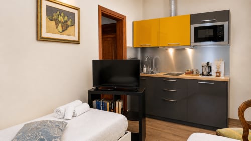 Suite moderna all'Al Battistero Luxury di Ravenna con letto, TV, angolo cottura con mobili gialli e elettrodomestici in acciaio inox