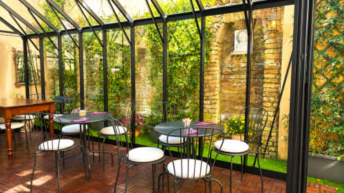 Sala da pranzo in veranda di vetro presso Al Battistero Luxury Suite a Ravenna con muri in laterizio ricoperto di edera e dettagli in metallo nero