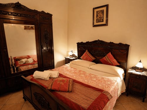 Elegant möbliertes Schlafzimmer im Harmoni Guest House in Siracusa mit dunklem Holzbett, roten Akzenten und warmer Beleuchtung