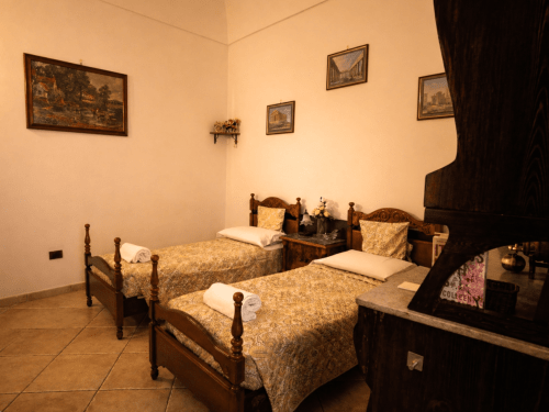 Doppelzimmer im Harmoni Guest House in Siracusa mit Holzbetten, Möbeln im Stil vergangener Zeiten und gerahmten Kunstwerken an pfirsichfarbenen Wänden