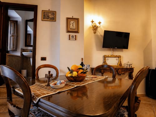 Elegantes Esszimmer des Harmoni Guest House in Siracusa mit Holztisch, Möbeln im Antikstil, Wandleuchten und an die Wand montiertem Fernseher