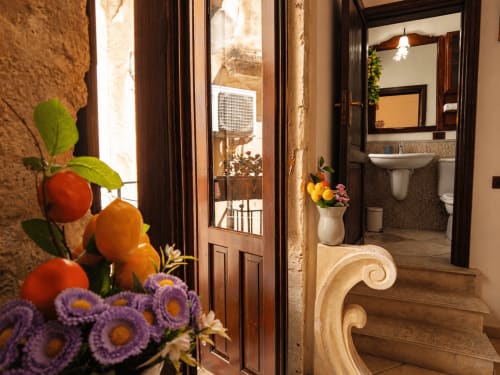 Eingang der Wohnung in Syrakus mit violetten Blumen, Badezimmertür, Treppe und Balkonblick im Harmoni Guest House