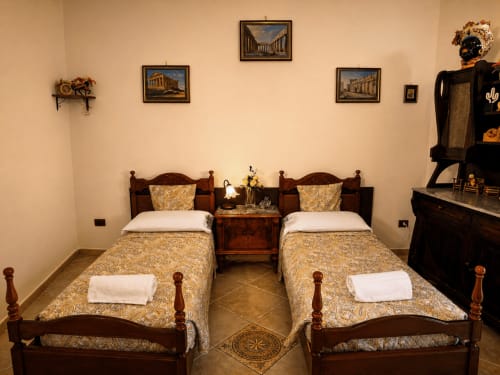 Doppelzimmer im Harmoni Guest House in Siracusa mit Holzbetten, goldener Bettwäsche und klassischen Kunstwerken auf cremefarbenen Wänden