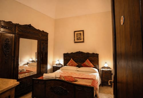 Elegantes Schlafzimmer im Harmoni Guest House Siracusa mit verziertem dunklem Holzmöbel, cremefarbener Bettwäsche, orangefarbenen Akzenten und Spiegeln