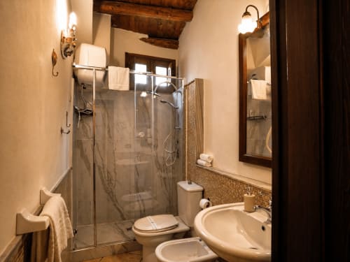 Elegante bagno presso la Harmoni Guest House di Siracusa con doccia in vetro, doppi lavabi e travi in legno rustico