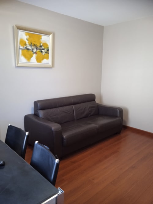 Studio moderne aux Balcons du Sancy avec canapé cuir noir, parquet et tableau abstrait jaune sur mur blanc