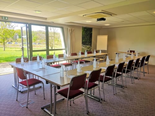 Salle de conférence moderne à l'hôtel La Verriaire avec table en U, vue sur parc verdoyant par grandes fenêtres
