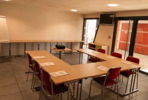 Salle de réunion moderne à l'hôtel La Verriaire à Chanverrie avec tables en bois, chaises rouges et équipements de présentation