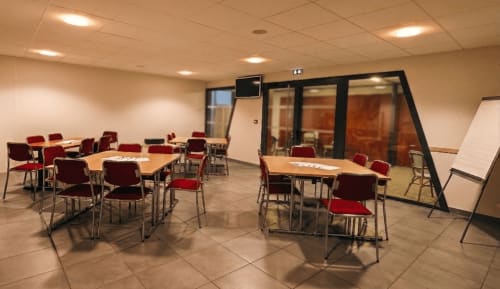 Salle de réunion moderne à l'hôtel La Verriaire à Chanverrie avec chaises rouges, tables en bois et tableaux de présentation