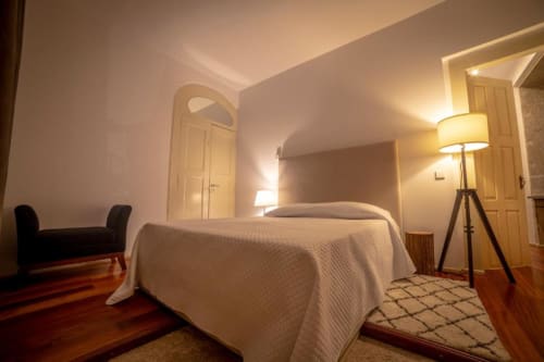 Quarto moderno do hotel Quinta da Malaposta em Valença com cama branca, piso de madeira e iluminação aconchegante