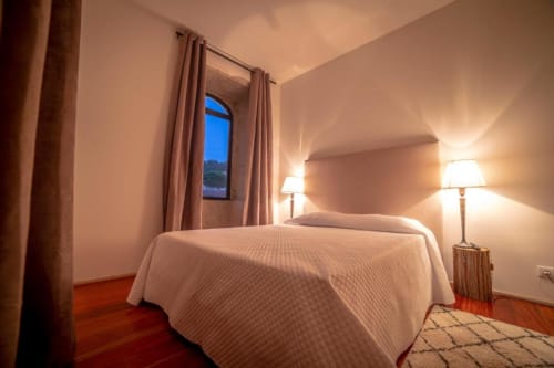 Quarto elegante na Quinta da Malaposta em Valença com cama de roupa branca, iluminação aconchegante e janela em arco com vista para o jardim