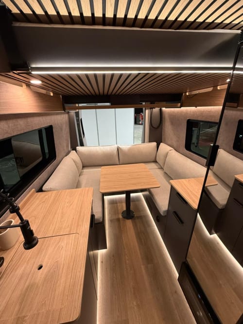 Lounge moderno de autocaravana con asientos crema, mesas de madera e iluminación LED en La Campera Space, Écija
