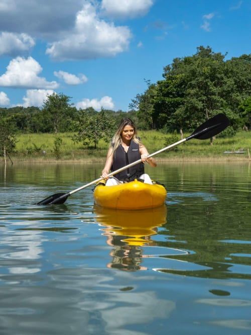 Mulher em caiaque amarelo no Chales do Lago, Caldas Novas, com floresta exuberante e céu azul ao fundo