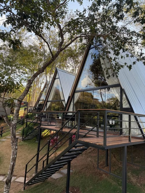 Chalé moderno em A-frame com janelas de vidro e varanda de madeira na Chales do Lago, Caldas Novas, cercado por vegetação exuberante