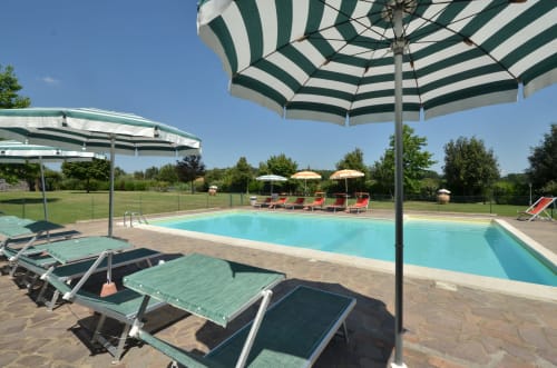 Espace piscine de l'Agriturismo Buriano à Lubriano avec transats, parasols rayés verts et jardins paysagés sous ciel bleu